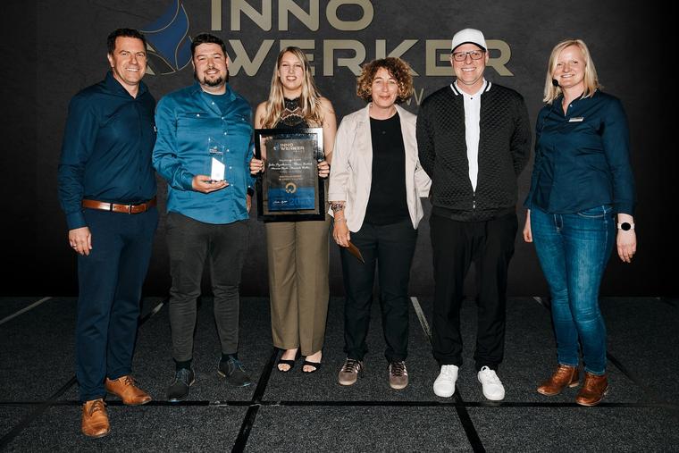 Preisverleihung des InnoWerker-Awards 2026: Kolleginnen und Kollegen von haushoch4 mit Urkunde und Glaspokal auf der Bühne, dahinter die Wand mit dem Logo des Wettbewerbs.